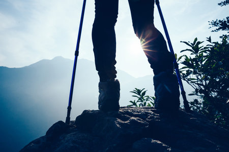 Successful hiker legs on mountain peak rock cliff edge