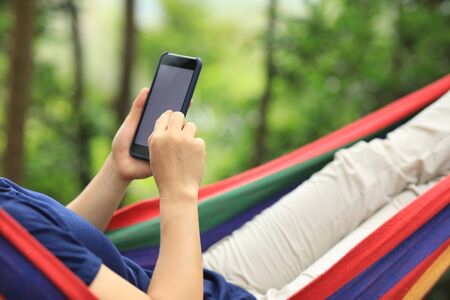 Relaxing in hammock with smartphone in forestの写真素材