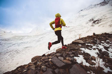 Woman trail runner cross country running up to winter snow mountain topの写真素材