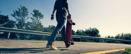 Skateboarder with skateboard walking on sunrise mountain peakの写真素材