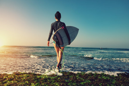 Woman surfer with surfboard going to surf at seaside