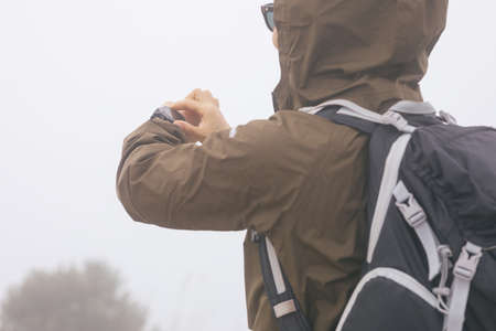 Woman hiker checking the altitude on her smartwatch at foggy mountain topの写真素材