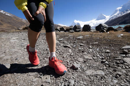 Woman runner with sports injured knee  running at high altitude mountain trailの写真素材