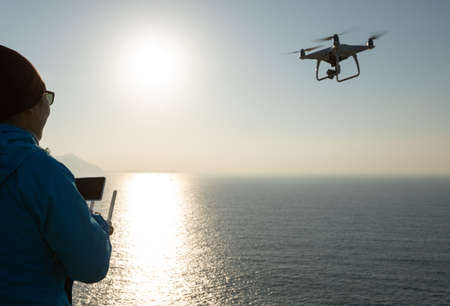 Silhouette of remote control a flying drone which taking photo over sunrise seaの写真素材