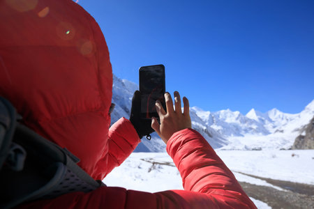 Woman hiker taking photo of glacier with smartphone in winter