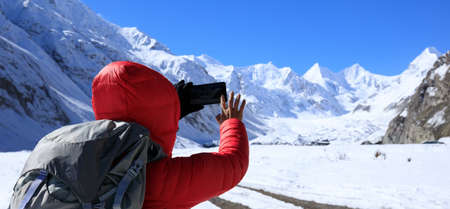 Woman hiker taking photo of glacier with smartphone in winterの写真素材