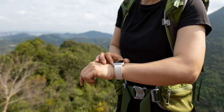Woman hiker checking on smartwatch on mountain topの写真素材