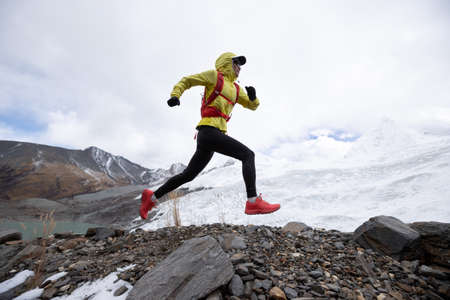 Woman trail runner cross country running up hill to winter snow mountain topの写真素材