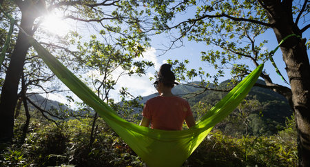 Relaxing in hammock hand using smartphone in tropical forestの写真素材