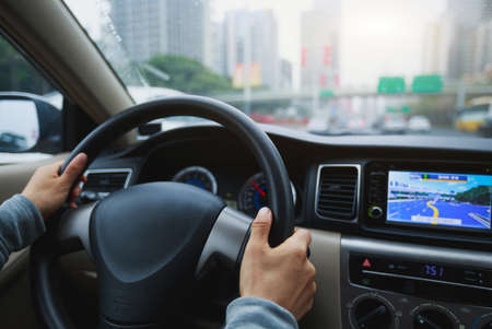 People hands holding steering wheel while driving car on city roadの写真素材