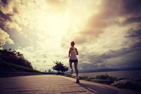 Fitness woman running on sunny coast trailの写真素材