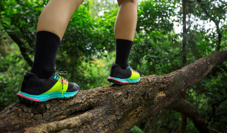 Sportswoman cross country trail runner legs waking on tree trunk in forest