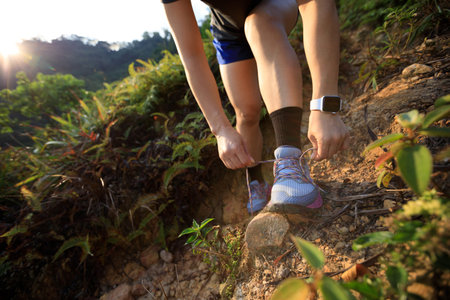 Woman runner tying shoelace on mountain trail