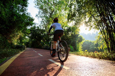 Woman cycling on bike path at sunrise parkの写真素材