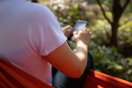 Relaxing in hammock hand using smartphone in tropical forestの写真素材
