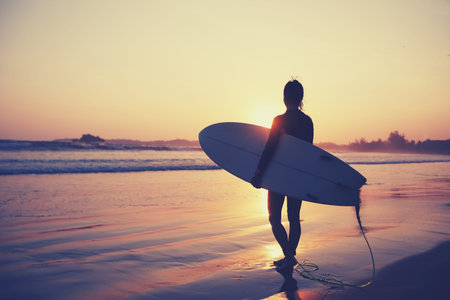 Woman surfer with surfboard on sunset beach