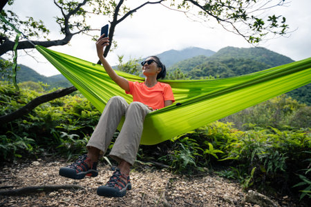 Relaxing in hammock hand using smartphone in tropical forest