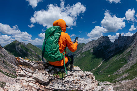 Successful woman backpacker using smart phone on alpine mountain top