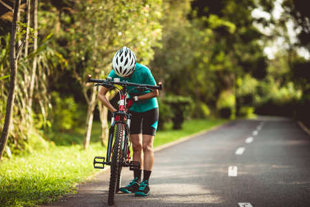 Woman cyclist adjust the seat height cycling on summer park trailの写真素材