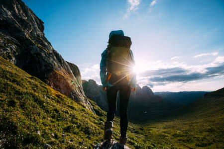 Successful woman backpacker hiking on sunset alpine mountain peakの写真素材