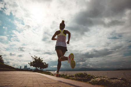 Fitness woman running on sunny coast trailの写真素材