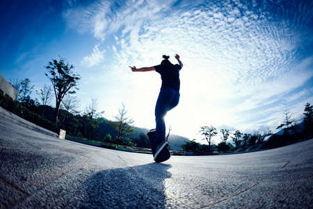 Asian woman skateboarder skateboarding in sunrise cityの写真素材