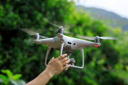 Hand reaching for a flying drone in summer forestの写真素材