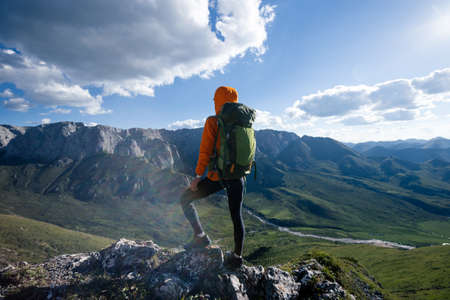 Successful woman backpacker hiking on sunset alpine mountain peakの写真素材