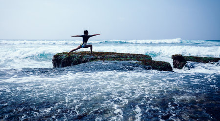 Woman practice yoga at seaside cliff edge facing the coming strong sea wavesの写真素材