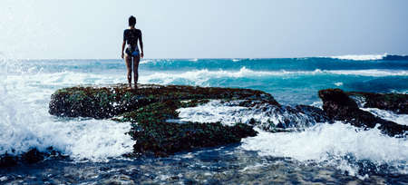 Woman at the seaside cliff edge facing the coming strong sea wavesの写真素材