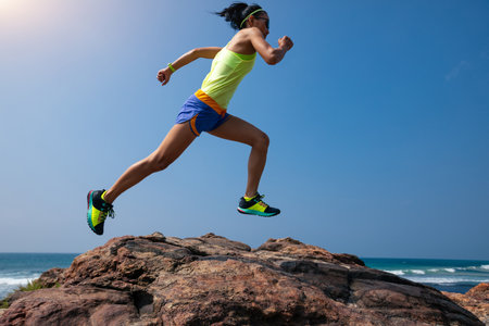 Young fitness woman trail runner running to rocky mountain top on seasideの写真素材