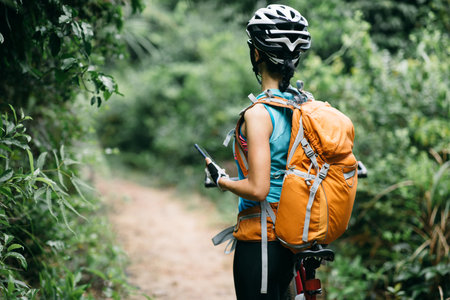 Woman cyclist use smartphone when riding mountain bike on forest trailの写真素材