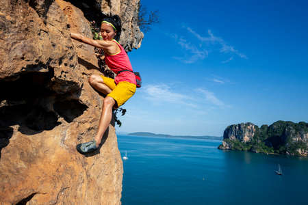 Young woman rock climber climbing on seaside cliffの写真素材