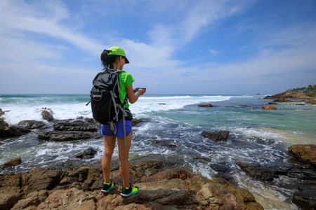 Young woman hiker using smartphone taking photo at seasideの写真素材