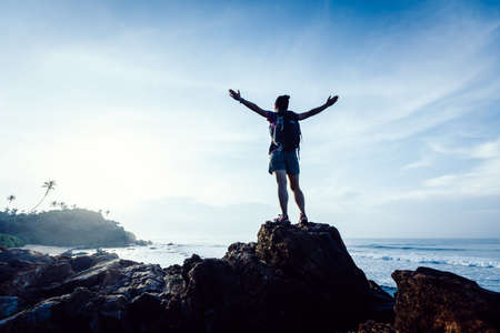 Strong woman outstretched arms on sunrise seaside rock cliff edgeの写真素材