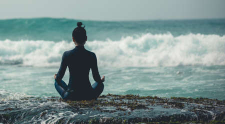Woman meditation at the seaside cliff edge facing the coming strong sea wavesの写真素材
