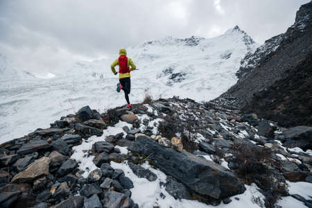Woman trail runner cross country running up to winter snow mountain topの写真素材