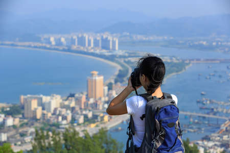 Young woman hiker taking photo with digital camera at mountain peakの写真素材