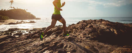 Woman trail runner running to rocky mountain top on sunrise seasideの写真素材