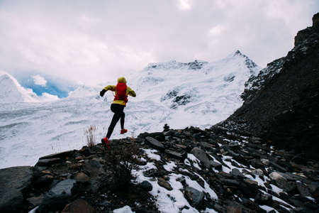 Woman trail runner cross country running up to winter snow mountain topの写真素材