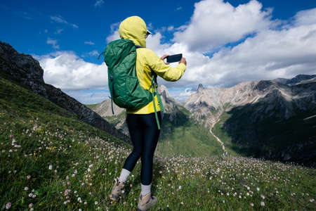 Successful woman backpacker using smartphone taking photo hiking on alpine mountain peakの写真素材
