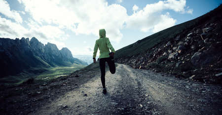 Woman ultramarathon runner stretching legs while running at mountain topの写真素材