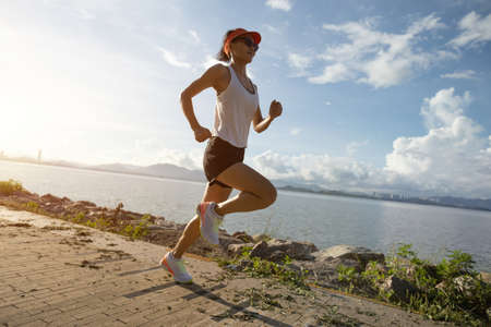 Fitness woman running on sunny tropical seasideの写真素材