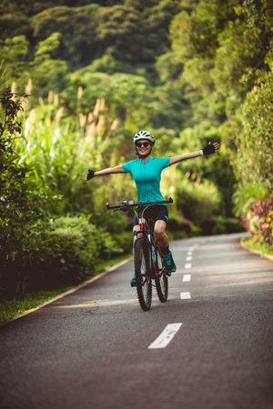 Woman no handed cycling on tropical park trail in summerの写真素材