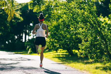 Fitness woman running on sunny tropical park trailの写真素材