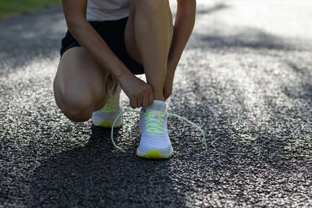 Woman runner tying shoelace on sunny tropical park trailの写真素材