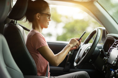 Woman using smartphone driving car on sunrise mountain roadの写真素材