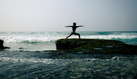 Woman practice yoga at seaside cliff edge facing the coming strong sea wavesの写真素材