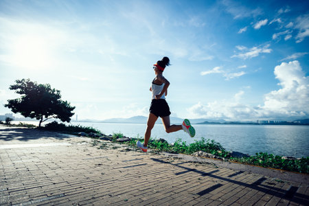 Fitness woman running on sunny tropical seasideの写真素材