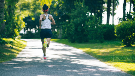 Fitness woman running on sunny tropical park trailの写真素材